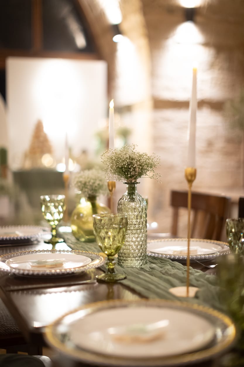 Long table laid with a sage runner, taper candles and gold glassware